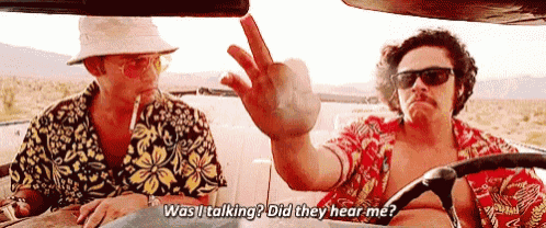 two men are sitting in a car and one of them is giving the middle finger while the other is smoking a cigarette .