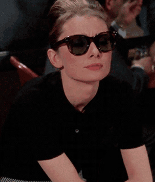 a woman wearing sunglasses and a black shirt is holding a cigarette