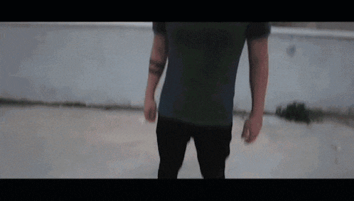 a man in a green t-shirt and black pants is standing in front of a wall