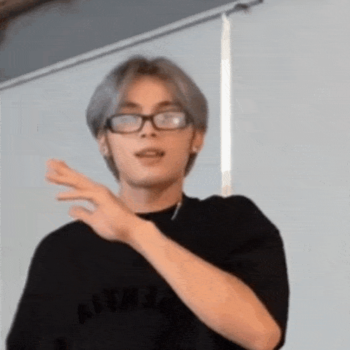 a young man wearing glasses and a black shirt is making a gesture with his hands .