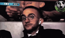 a man wearing glasses and earbuds is watching a soccer game