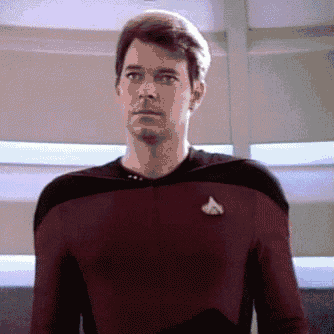 a man in a red and black uniform is standing in a room and looking at the camera .