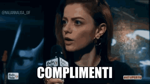 a woman is talking into a microphone and the word complimenti is visible