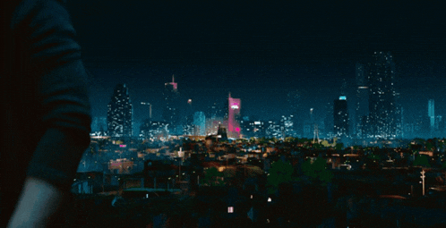 a person looking at a city skyline at night with a pink building in the foreground