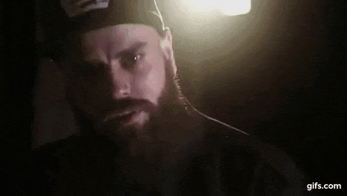 a man with a beard wearing a hat is giving a thumbs up in the dark .