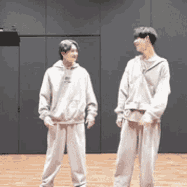 two young men are standing next to each other on a wooden floor in a room .