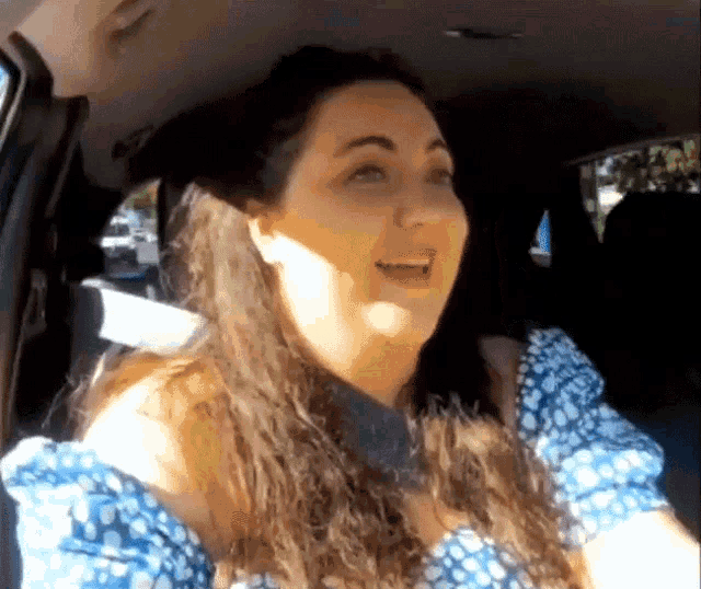 a woman in a blue dress is sitting in a car and smiling