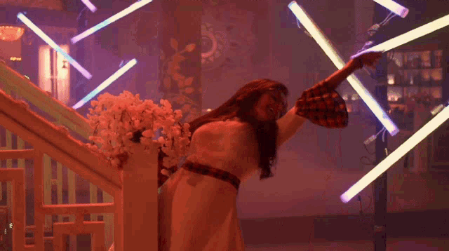 a woman with long hair and glasses stands in front of flowers in a dark room