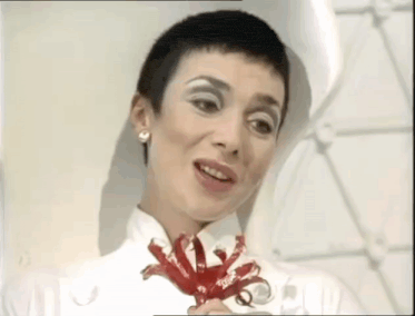 a woman with short hair is holding a red flower .