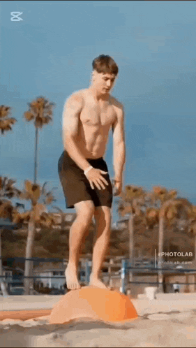 a shirtless man is jumping over a small orange object on the beach .