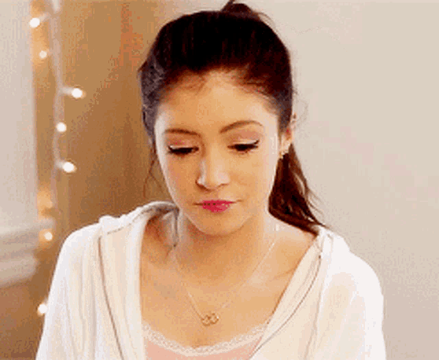 a woman wearing a white hoodie and a pink tank top is looking down