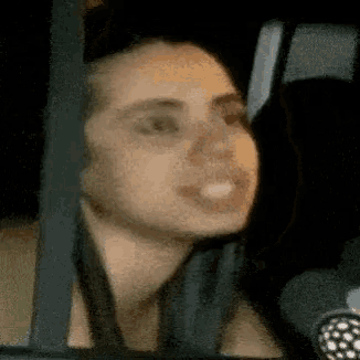 a woman is sitting in a car looking out the window and smiling .