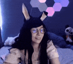a woman wearing bunny ears and glasses is sitting on a bed with a stuffed panda in the background .