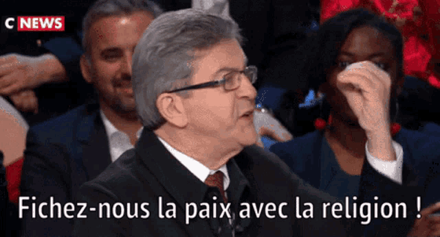 a man in a suit and tie is sitting in a crowd with the words " fichez-nous la paix avec la religion " above him
