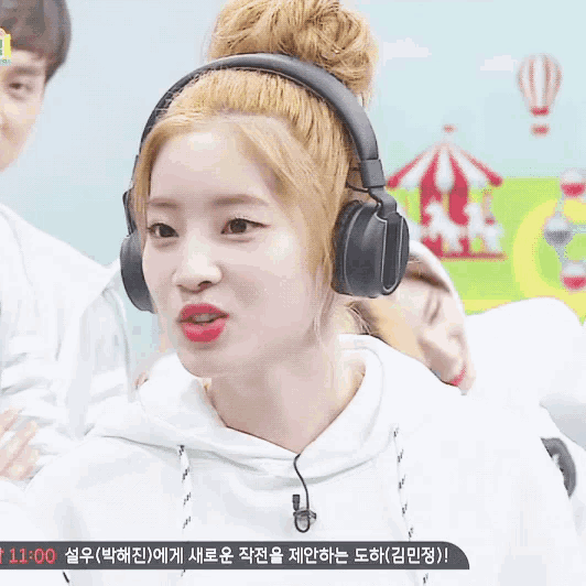 a woman wearing headphones looks at the camera with a time of 11:00 behind her