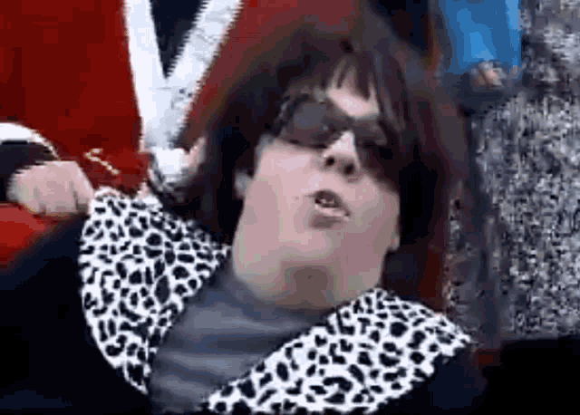 a woman wearing sunglasses and a leopard print jacket is making a face .