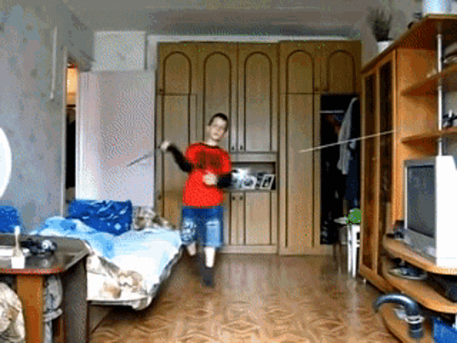 a boy in a red shirt is holding a stick in a living room