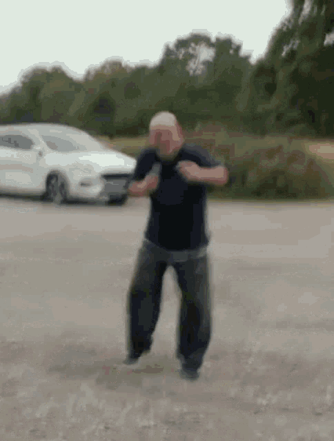 a man is dancing in a parking lot next to a white car .