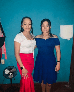 two girls pose for a picture in front of a blue wall and a fan