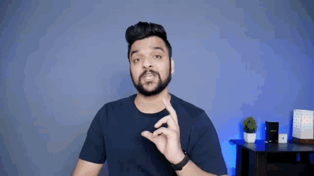 a man with a beard is standing in front of a blue wall and making a gesture with his hand .
