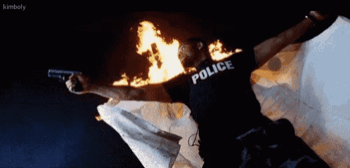 a police officer is holding a gun in front of a flag that is on fire .