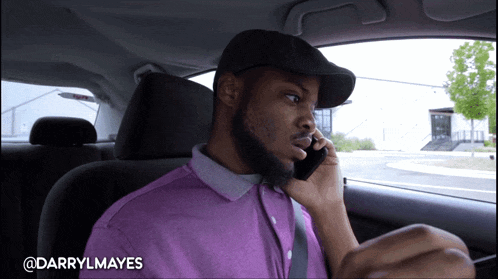 a man in a purple shirt is talking on a cell phone while sitting in a car