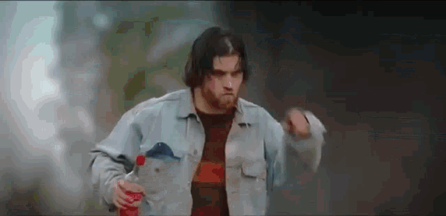 a man in a denim jacket is holding a bottle of coca cola and dancing .