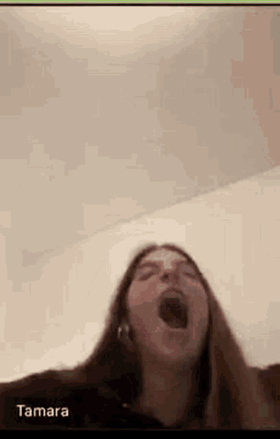 a woman is yawning on a video call while wearing a headset .