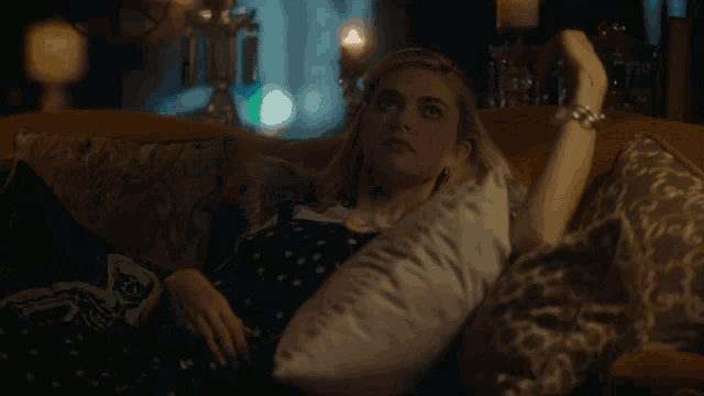 a woman in a black dress is laying on a couch with pillows