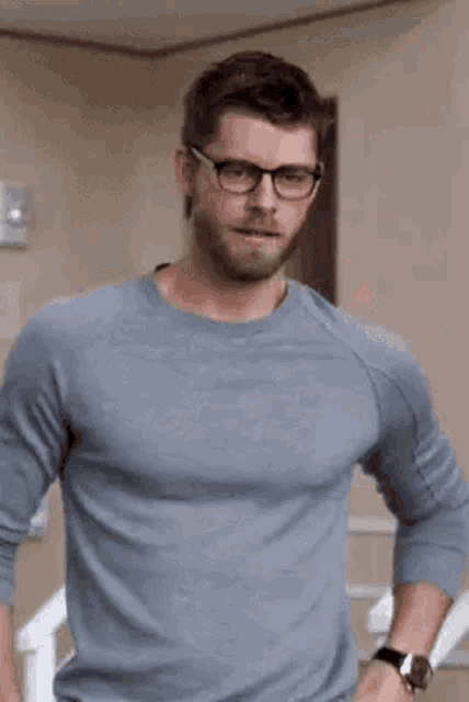 a man with glasses and a beard is standing with his hands on his hips .