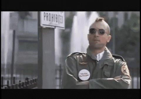 a man wearing sunglasses and a mohawk stands in front of a sign that says prohibited