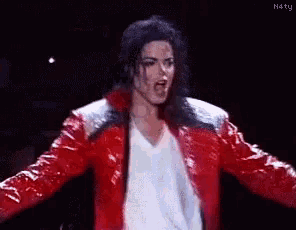 a man in a red jacket and white shirt is standing on a stage .