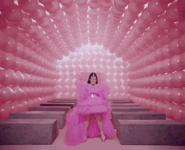 a woman in a pink dress is standing in a room filled with pink balloons