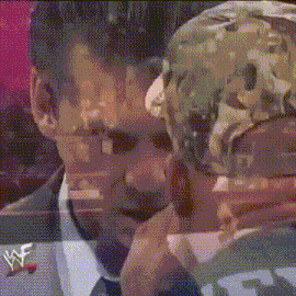 a man in a suit and tie is holding a person 's head with a wwe logo on his jacket .