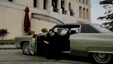 a man in a black suit is getting out of a green car
