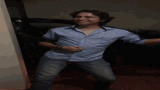 a man in a blue shirt and jeans is dancing in a dark room