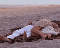 a man and woman laying on a blanket on a beach