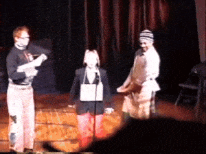 a group of people standing on a stage with one wearing a hat