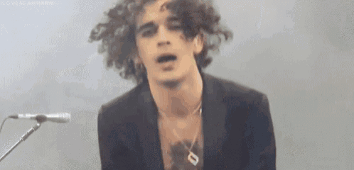 a young man with curly hair is singing into a microphone while playing a guitar .