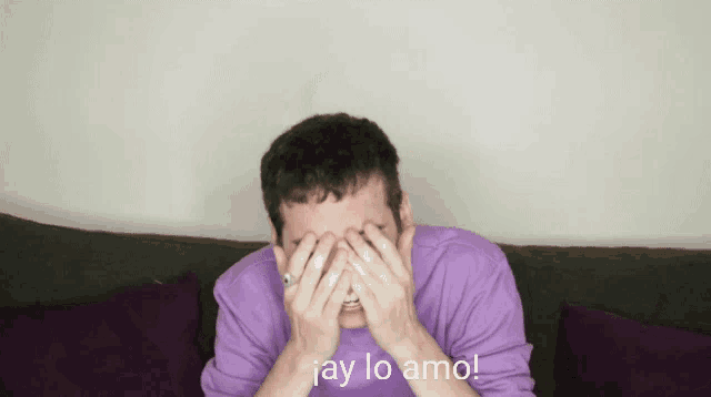 a man in a purple shirt is covering his face with his hands and the words " ay lo amo " written below him