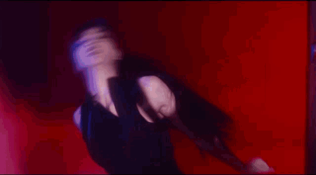 a woman in a black dress is dancing in front of a red wall .