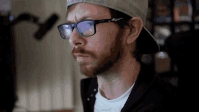 a man with a beard and glasses is wearing a hat and looking at something .