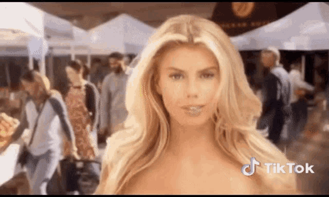 a woman without a shirt is standing in front of a crowd of people and a sign that says tik tok