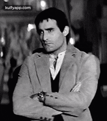 a man in a suit and tie is standing with his arms crossed in a black and white photo .