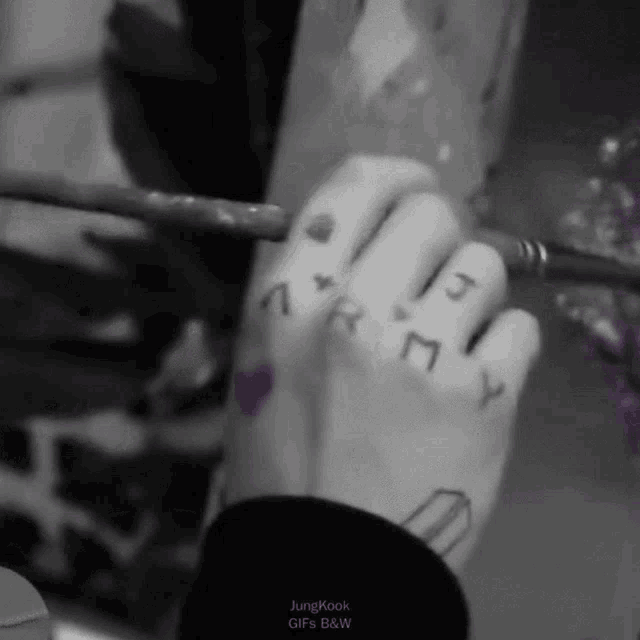 a black and white photo of a person 's hand with a brush and a tattoo on it .