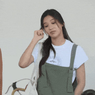 a woman wearing overalls and a white t-shirt that says ' jesus is coming ' on it