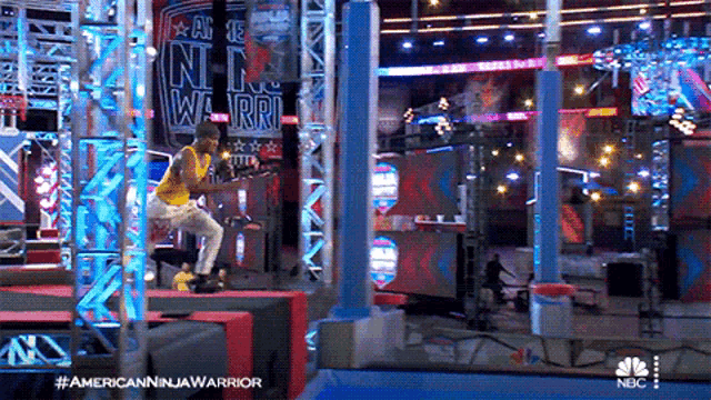 a man in a yellow shirt is sitting on a bench in front of an american ninja warrior sign
