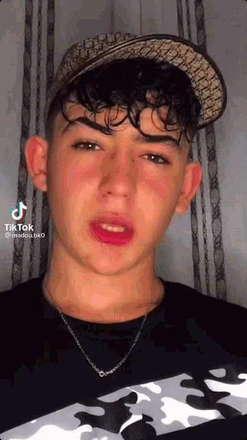 a young man wearing a hat and a necklace has a tiktok on his face