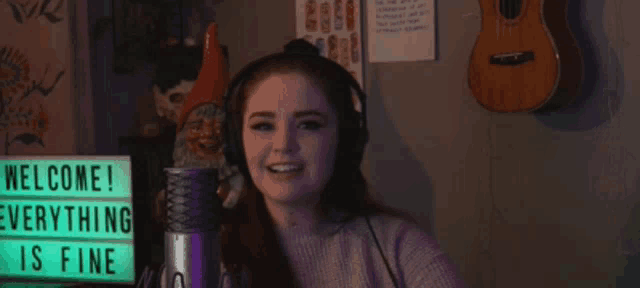 a woman wearing headphones stands in front of a sign that says " welcome everything is fine "