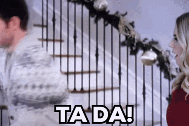 a man and a woman are standing next to each other on a set of stairs and the woman is saying ta da .
